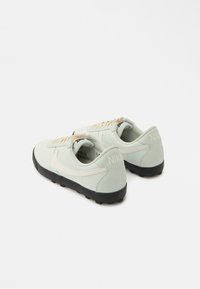 Ανοιχτό πράσινα αθλητικά παπούτσια Nike με λείο υφή, μαύρη εξωτερική σόλα και κρεμ χρώματος λεπτομέρειες. Διαθέτουν διακριτικό λογότυπο στη φτέρνα και στα κορδόνια.