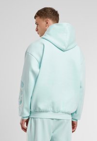 Sudadera verde menta con un ajuste holgado, presenta un capucho con cordón y elementos de diseño texturizados en las mangas. Material de suave mezcla de algodón.