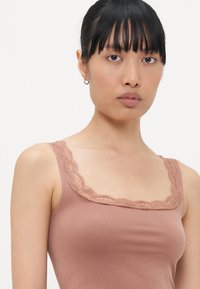 Bruine tanktop met een kantafwerking bij de halslijn, gemaakt van een gladde, rekbare stof. Heeft dunne schouderbandjes.