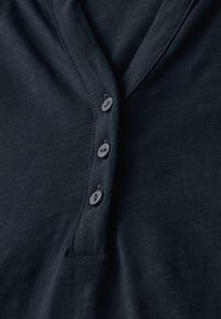 Mörk marinblå tröja i jersey med V-ringning och fyra grå knappar längs knappslån. Slät textur med en subtil glans.