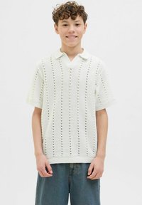 Vit stickad kortärmad polo med V-ringning, med hålmönster och ribbade cuffs och nederkant, bärs med blå denimshorts.