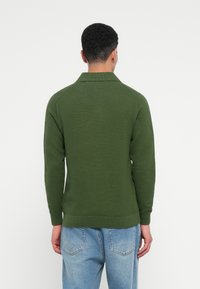 Sötétzöld, textúrált pulóver, galléros nyakkivágással és bordázott mandzsettákkal. A pulóver egyenes aljjal és laza fazonnal rendelkezik.