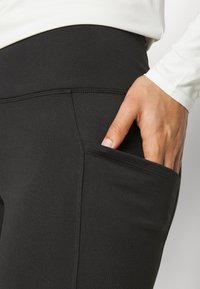 Zwarte legging gemaakt van rekbaar materiaal, met een zijzak en een naadloos ontwerp. Glad oppervlak met een hoge tailleband.