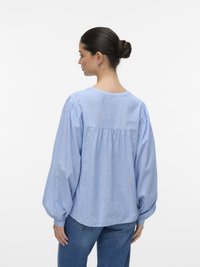 Lyseblå, stripete bluse med puffede ermer, rund halslinning og samlet detalj bak, kombinert med denimjeans.