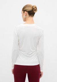 Maglietta bianca a maniche lunghe, aderente, con scollatura rotonda e dettagli arricciati sul retro, abbinata a pantaloni bordeaux a vita alta.