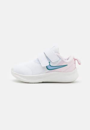 Zapatilla deportiva blanca con parte superior de malla, dos correas de Velcro y acentos en teal y rosa. Suela redondeada para soporte y agarre.