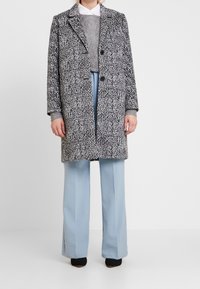 Szary wzorzysty płaszcz z wyłogowym kołnierzem, dwoma przednimi guzikami i szarymi mankietami; narzucony na szary sweter i jasnoniebieskie szerokie spodnie.