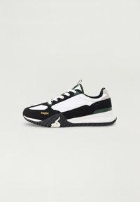 Zapatilla deportiva en blanco y negro con acentos verdes y grises, que presenta una suela texturizada, un diseño de cordones y un logo de marca en el costado.