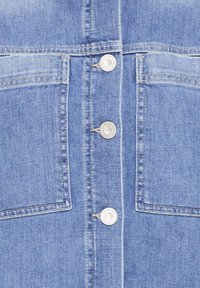 Denim overhemd met een lichtblauwe kleur, twee borstzakken en metalen knopen aan de voorkant voor sluiting. De textuur is glad en klassiek.