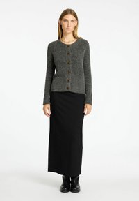 Cardigan grigio a maglia con collo tondo e sette bottoni marroni, abbinato a una gonna nera lunga e stivaletti neri. Texture liscia, stile casual.