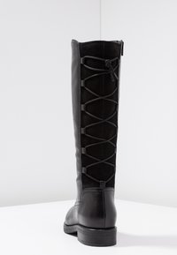 Bota negra de cuero y ante hasta la rodilla, con punta lisa, parte trasera texturizada con cordones y un tacón bajo y cuadrado. Cierre con cremallera en el lateral.