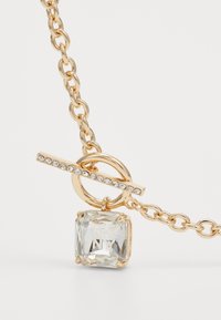 Collier en chaîne dorée avec un pendentif en cristal transparent carré gravé "DKNY" et un fermoir en or en forme de bascule rehaussé de petites pierres transparentes.