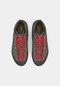 Scarpe da trekking grigie con lacci rossi e occhielli metallici. Presentano una tomaia texturizzata e suole in gomma resistente per una buona aderenza. Suole interne con doppio marchio visibile.