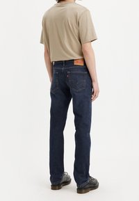 Beige t-shirt med kort ärm som kombineras med mörkblå raka jeans. Märkbart baklapplabel och klassiska fickstickningsdetaljer.