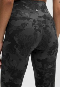 Černé legíny s vysokým pasem a texturovaným květinovým vzorem, vyrobené z pružné tkaniny, s švem vzadu a detailním logem značky.