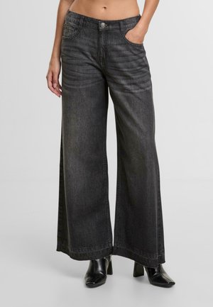 Wijdere jeans in donkergrijs denim met een zachte textuur. Kenmerken zijn onder meer voorzakken, een knoopsluiting en subtiele verticale stiksels.