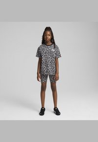 Conjunto de camisa de manga corta y pantalones cortos con patrón en blanco y negro, hecho de una tela suave, combinado con zapatillas deportivas negras, de pie contra un fondo gris.