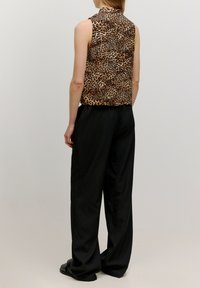 Ärmelloses Top mit Leopardenmuster aus glattem Stoff, kombiniert mit schwarzen, lockeren Hosen. Beide Teile zeichnen sich durch ein schlichtes Design aus.