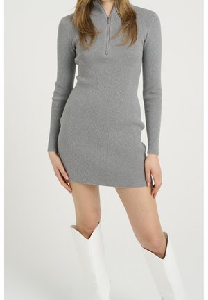 Schmal geschnittenes, geripptes Kleid in Hellgrau mit langen Ärmeln und Halb-Reißverschluss am Kragen. Kombiniert mit hohen, weißen Stiefeln. Einfaches und modernes Design.