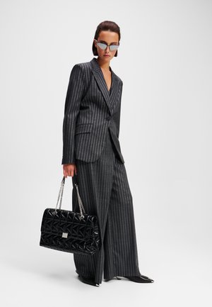 Completo a righe nere con giacca aderente e pantaloni a gamba larga. Gli accessori includono una borsa nera trapuntata con tracolle a catena e occhiali da sole angolari.