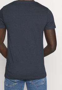 Navy blue cotton t-shirt with short sleeves, round neck, and a smooth texture. Fitted design, shown from the back, paired with denim jeans.