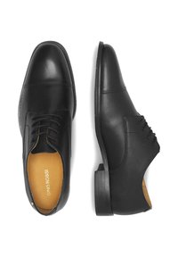 Melnas ādas kleitu kurpes ar noapaļotu purngalu, aukliņu dizainu, kontrastējošām šuvēm un pl�ānu, teksturētu zoli. Iekšpuse ir brūngana.