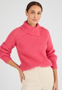 Maglione rosa a maglia con colletto alto e ripiegato, texture a coste e maniche lunghe, abbinato a pantaloni in velluto a coste di colore crema.