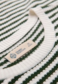 Suéter de punto con rayas verdes y blancas, con un escote acanalado y una etiqueta con la inscripción "Ombre Heritage M" cosida.