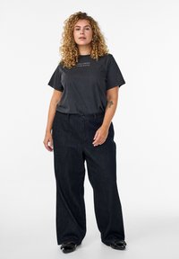 Camiseta de algodón negra con mangas cortas y gráfico de texto, combinada con pantalones vaqueros oscuros de corte holgado y zapatos planos negros con tachuelas.