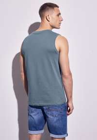Top in cotone teal senza maniche con una vestibilità comoda. Abbinato a pantaloni shorts in denim blu con risvolti e tasche posteriori.