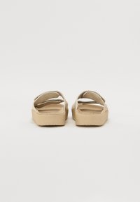Beiga öppna sandaler med dubbla remmar och texturerade gummisulor. Designen har en minimalistisk stil och mjukt mockaliknande material.
