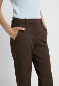 Bruine op maat gemaakte broek van soepel stof, met zijzakken, een platte voorkant en een slim fit. Gemaakt met een lichtblauw gestructureerd bovenstuk.