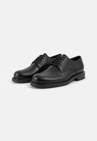 Chaussures habillées en cuir noir avec un bout rond, un design à lacets, une texture lisse et une silhouette minimaliste. Semelle noire robuste et accents subtils.