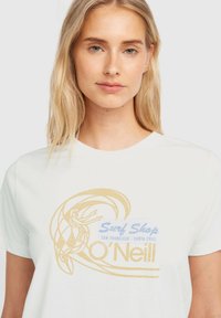 White cotton t-shirt featuring a retro surf shop graphic in gold and blue, depicting a surfer and wave design. Short sleeves and crew neck.