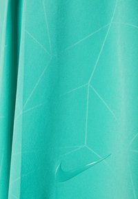 Tejido atlético turquesa con un patrón geométrico y textura suave, con un logo brillante de Nike en la esquina inferior derecha.