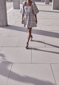 Kort klänning med fyrkantig ringning, puffärmar och geometriskt mönstrad tyg i blått och vitt. Bärs med lätta blå sandaler med remmar.