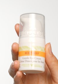 Burt's Bees Mild Øyekrem i en hvit og oransje flaske med en klar heksagonal-mønstret kork. Inneholder 15 ml, merket for sensitiv hud.