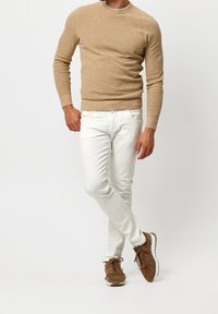 En tanfärgad stickad tröja, vita slim-fit byxor och bruna mockaskor. Tröjan har en rund halsringning; skorna har en texturerad yta.