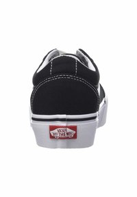 Zapatilla baja de lona negra con suela de goma blanca, acentos en blanco y negro, y una etiqueta del logo rojo de Vans en el talón.