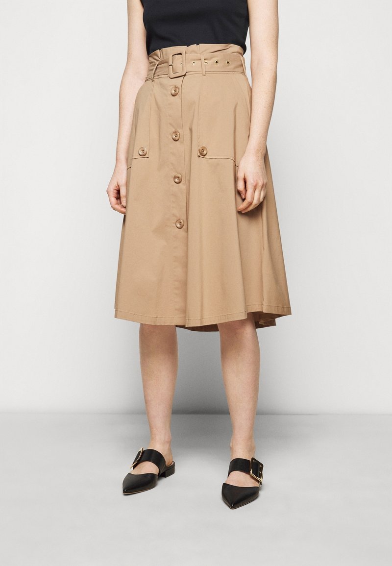 Lichtbruine midi-rok met een ceintuur in de taille, knoopsluiting aan de voorkant en twee grote zijzakken. Draag het met zwarte puntige flats met een gouden accent.