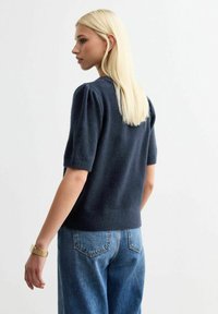 Maglione corto blu navy a maniche corte con spalle a sbuffo e texture fine, abbinato a jeans blu a vita alta. Design semplice e casual.