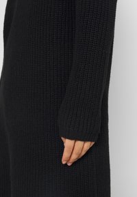 Lång svart stickad tröja med en strukturerad mönster, med standardpassform, ribbade ärmslut och synliga sömmar på sidan.