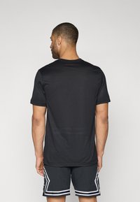 T-shirt de sport noir à manches courtes avec une texture lisse et un design classique à col rond, porté avec un short noir à motifs avec des accents blancs.