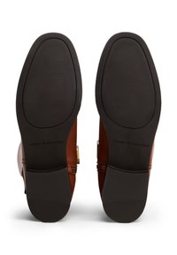 Brune lærstøvelsåler med en strukturert sort gummibunn. "TOMMY HILFIGER" trykt på siden. Har en liten kurve nær tåen.