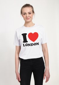 Bílá bavlněná tričko s velkým černým symbolem „I“ a červeným srdcem, pod nímž je nápis „LONDON“ tučně psanými černými písmeny. Volný střih.