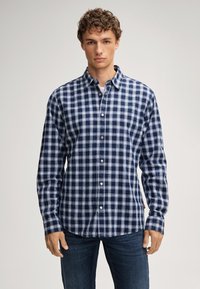 Camicia a quadri blu e bianca con colletto, maniche lunghe e taschino a sinistra sul petto, abbinata a jeans in denim.