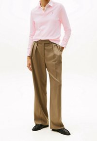 Polo shirt rosa chiaro a maniche lunghe con scollatura a V, abbinato a pantaloni brown a vita alta e pieghe, e mocassini neri. Tessuto morbido, vestibilità su misura.