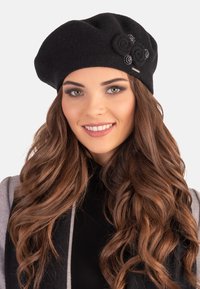 Beret de lana negra con tres rosetas de tela y un sutil acento metálico. Textura suave con un diseño redondeado y holgado.