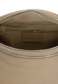 Interiér béžové kožené tašky se zipovou kapsou, podšívkou z látky a vyšitým logem. Stříbrný zipový kovový prvek, texturovaný povrch.