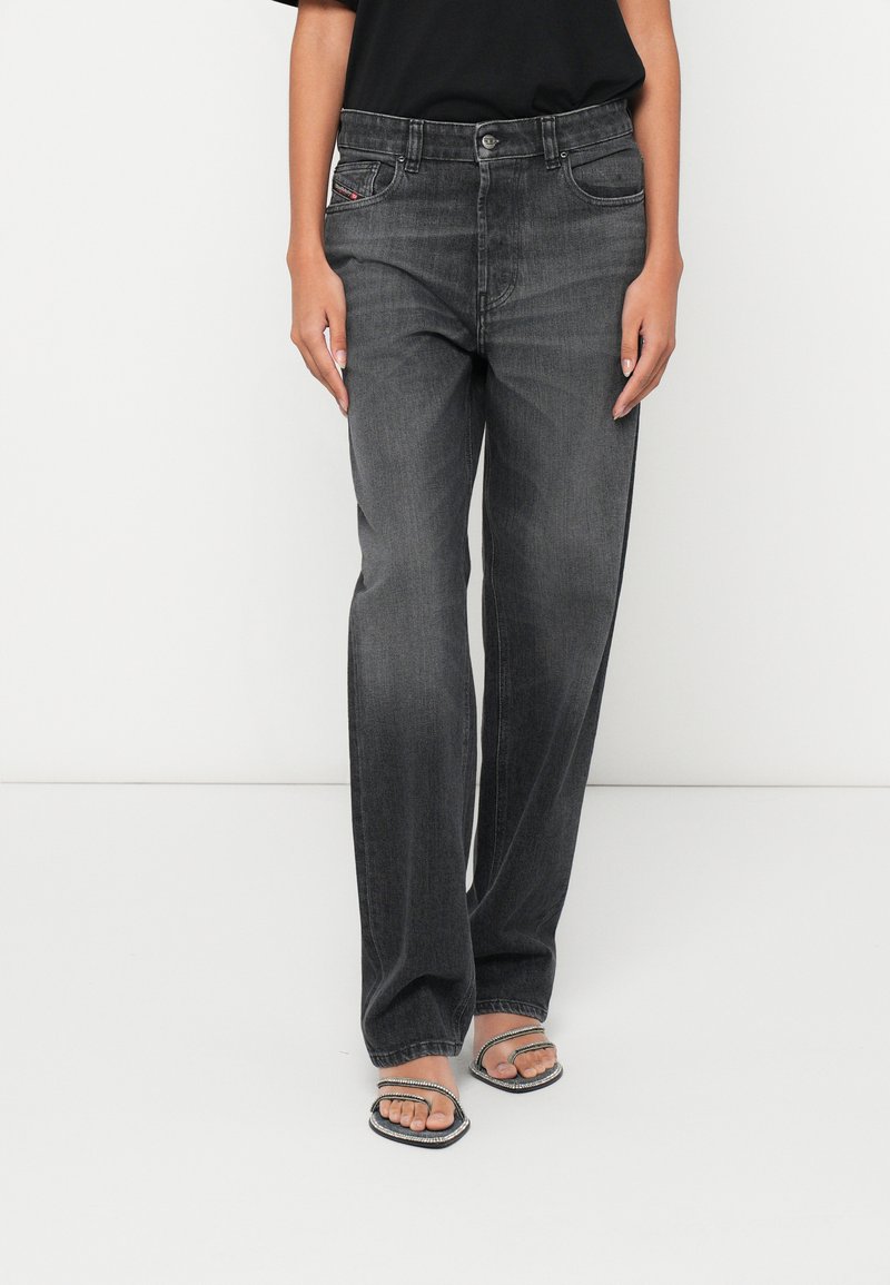 Augsta vidukļa, taisnas melnas džinsa bikses ar smalku izbalējušu apdari, metāla pogu aizdari un klasisku piecu kabatu dizainu.